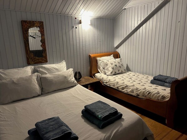 Un dormitorio con dos camas, cabeceros de madera, una mesita de noche y una lámpara fijada a la pared.
