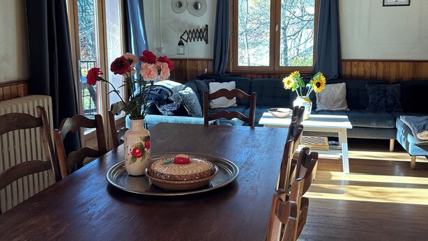 Una mesa de madera con sillas, un florero con flores y un pastel sobre una bandeja.