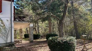 Una cabaña rústica con cimientos de piedra, una terraza de madera y un balcón con vistas a un bosque.
