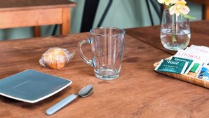 Une table avec une carte du monde, une tasse en verre, un vase avec des fleurs, un muffin, un téléphone intelligent, une cuillère et un plateau contenant des sachets de thé vert.