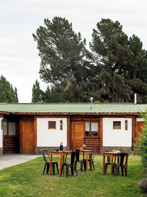 Una cabaña rústica con techo verde, puertas de madera y un pequeño porche con sillas y una mesa.
