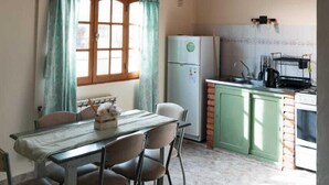 Une cuisine rustique avec des poutres en bois, une table à manger avec des chaises, un réfrigérateur et un buffet vert.