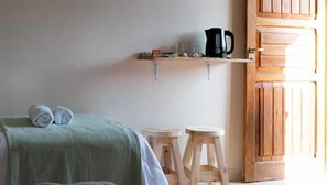 Une chambre avec deux lits, un téléviseur fixé au mur, une porte en bois et un petit coin cuisine équipé de tabourets.