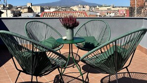 Een terras met twee groene stoelen en een tafel, met uitzicht op een stadsbeeld met een berg in de verte.