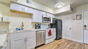 Une cuisine compacte avec des meubles blancs, un réfrigérateur en acier inoxydable, un four à micro-ondes, une cuisinière et un évier.