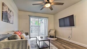 Un salon avec un ventilateur de plafond, un téléviseur fixé au mur, un canapé, une table basse et un fauteuil.