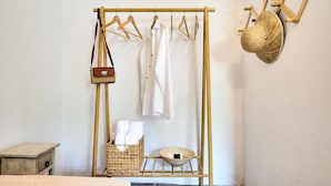 A room with a wooden drying rack holding clothes and a hat, a wicker basket with towels, and a small wooden table. - Apartments Panethimos (Platanias)
