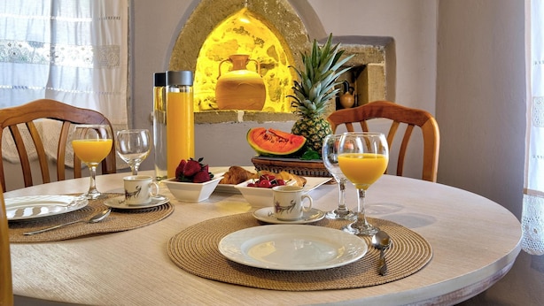 A breakfast setting with a table set for two, featuring plates, glasses, and a bowl of fruit. - Apartments Panethimos (Platanias)
