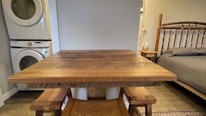 Una mesa de madera con bancos, una lavadora, una cama y un tapete estampado en una habitación.