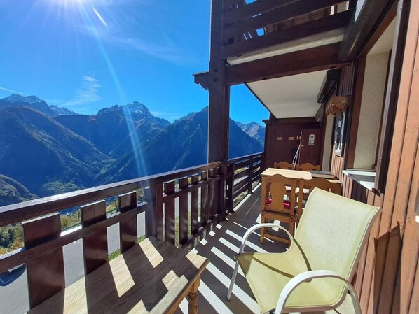 A balcony with a view of mountains, wooden furniture, and a wooden railing.