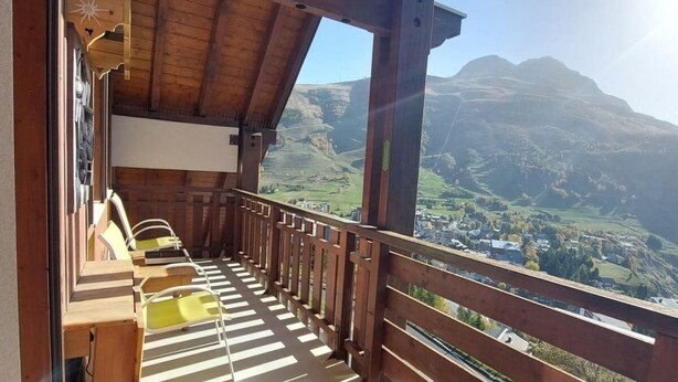 Uma varanda com guarda-corpo de madeira, vista para uma paisagem montanhosa e área de estar com cadeiras e mesa.