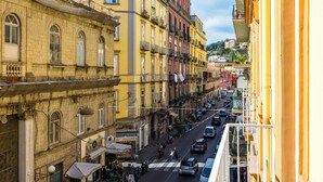 A street view of a historic European town with multi-story buildings, a pedestrian crossing, and parked cars.