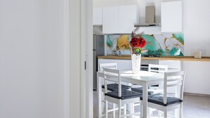 A modern kitchen with white cabinetry, a wooden countertop, and a decorative backsplash. There is a white dining table with four chairs and a vase with red flowers on the countertop.