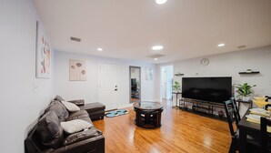 A modern living room with a leather sofa, a round coffee table, a flat-screen TV, and a dining area with a table set for two. - Cozy 2BR Quincy Hideout • Pet-Friendly • Wollaston Beach & Red Line 74L (Quincy)
