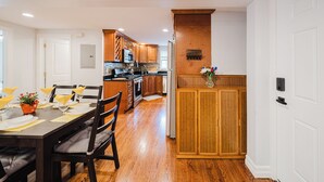 A modern kitchen with wooden cabinets, a central island, and a dining area with a table set for four. - Cozy 2BR Quincy Hideout • Pet-Friendly • Wollaston Beach & Red Line 74L (Quincy)
