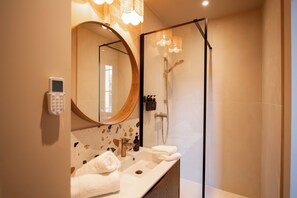 Une salle de bain moderne avec un grand miroir rond, un lavabo et une douche à parois de verre.