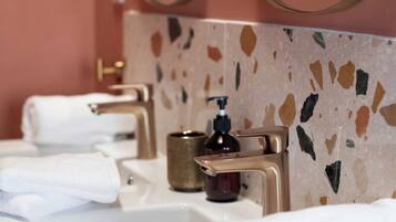A bathroom with three sinks, each with a towel. There are gold faucets and a soap dispenser on the counter.