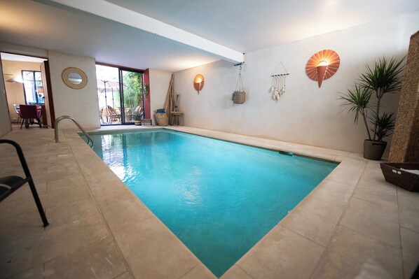 Une piscine intérieure à l’eau claire, un cadran solaire et une petite table avec des chaises.