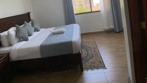 Ein Hotelzimmer mit Bett, Nachttisch, einem Fenster mit Vorhängen und Blick auf Gebäude.