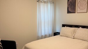 A bedroom with a large bed, a dark-colored armchair, a window with curtains, and two framed pictures on the wall. - Charming 3-bedroom home with WiFi, King bed in fabulous Copperas Cove (Copperas Cove)