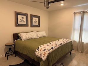 A bedroom with a bed, a small table, two framed pictures on the wall, a ceiling fan, and a window with curtains. - Charming 3-bedroom home with WiFi, King bed in fabulous Copperas Cove (Copperas Cove)