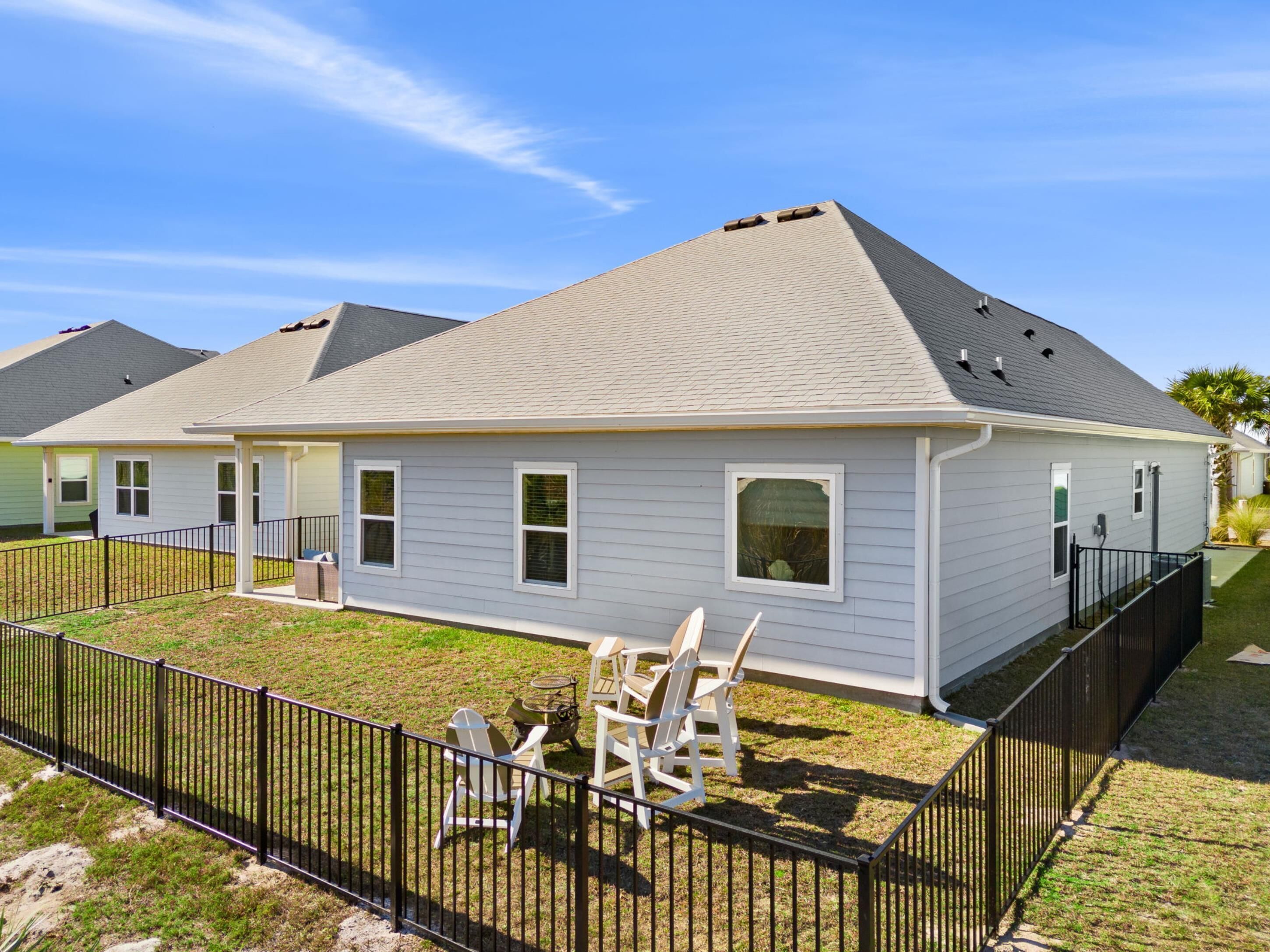 A single-story house with a sloped roof, a fenced backyard, and outdoor furniture.