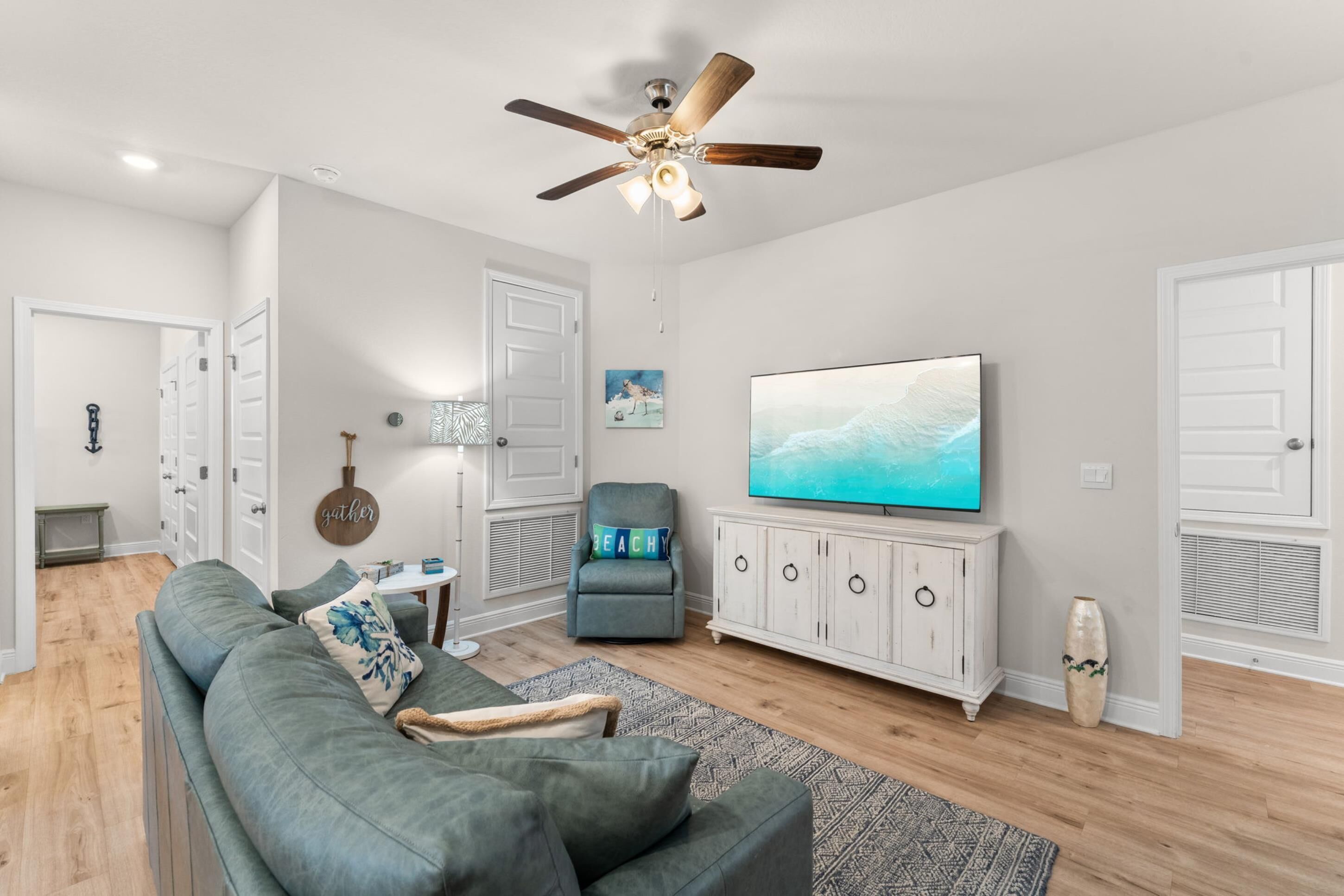 Un salon moderne avec un canapé gris, un ventilateur de plafond, un téléviseur et un meuble.