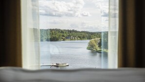 Une vue à travers une fenêtre sur un lac, avec un quai et un bateau, le tout entouré d’arbres et de bâtiments.