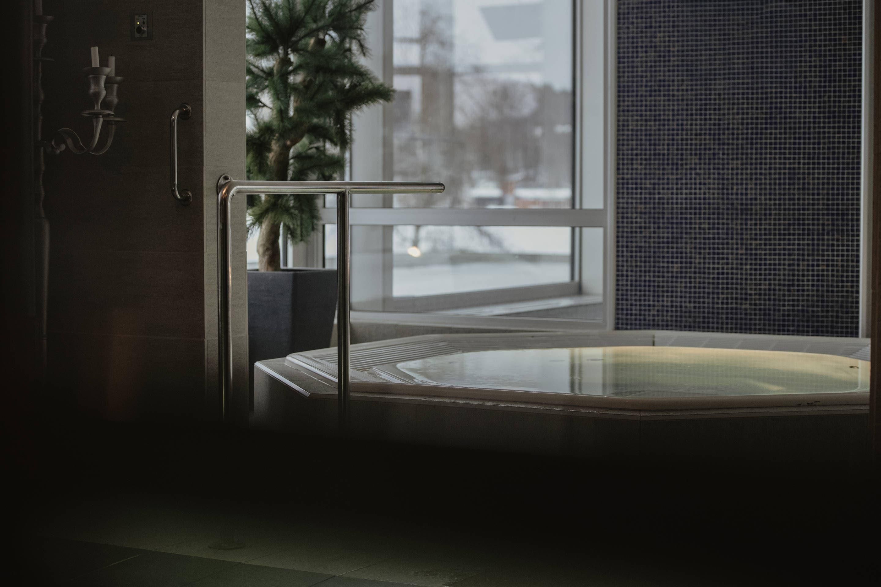 A modern bathroom with a glass-enclosed hot tub, a potted plant, and a view of the outside.