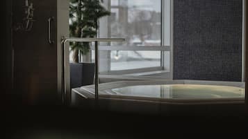 A modern bathroom with a glass-enclosed hot tub, a potted plant, and a view of the outside.