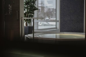 A modern bathroom with a glass-enclosed hot tub, a potted plant, and a view of the outside. - Hernö Gin Hotell (Harnosand)