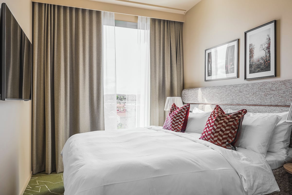 Une chambre d’hôtel avec un grand lit, une vue sur la ville et deux tableaux encadrés au mur.