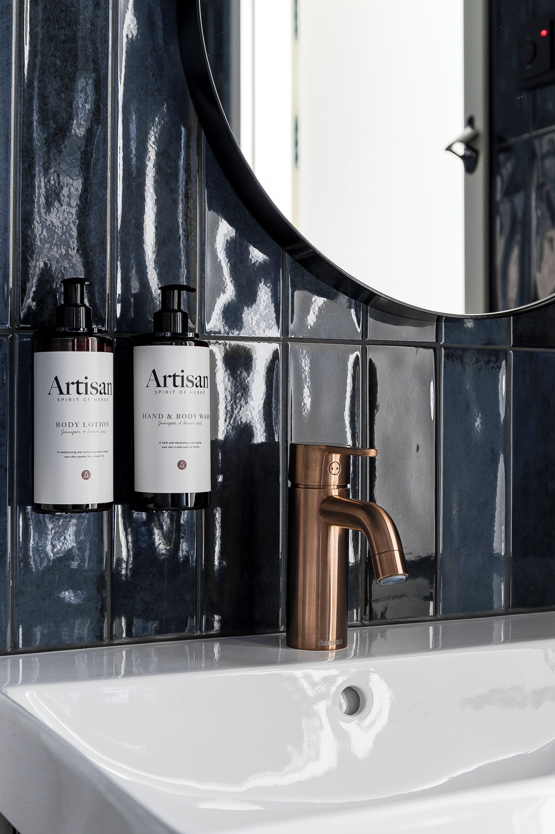 A bathroom with a white sink, two bottles of Artisan body lotion, and a copper faucet.