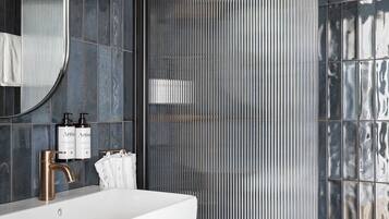 Un baño moderno con un lavabo blanco, un espejo grande y una zona de ducha con separador metálico acanalado.