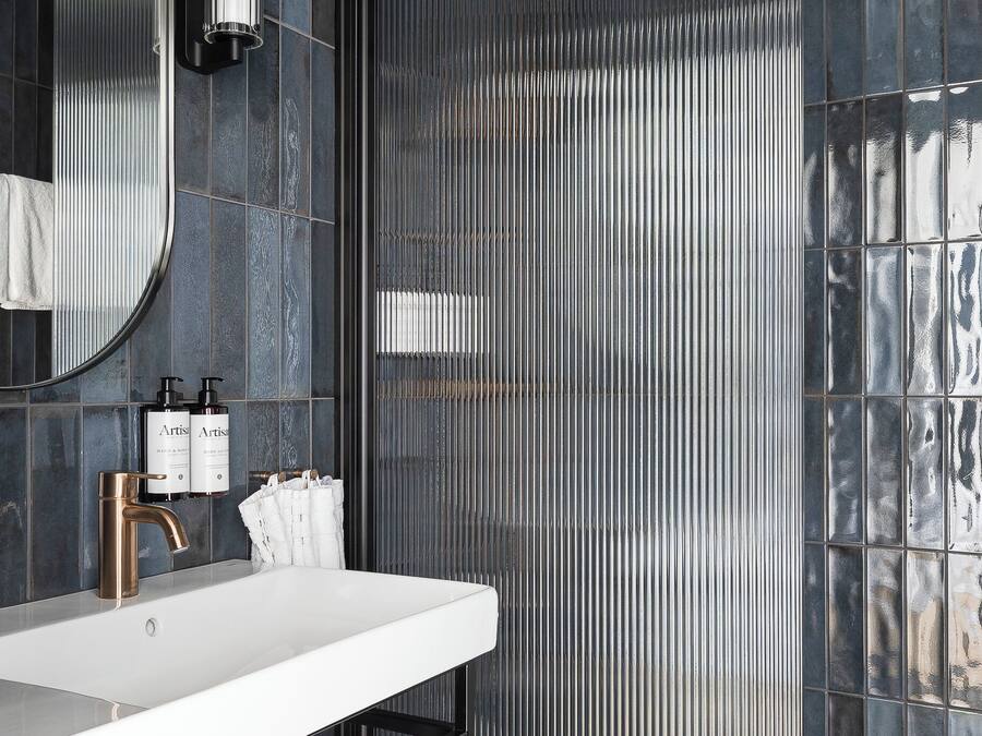 Un baño moderno con un lavabo blanco, un espejo grande y una zona de ducha con separador metálico acanalado.