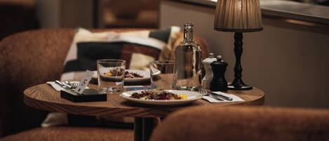 A dining table with plates, glasses, cutlery, and a lamp in a dimly lit room with upholstered chairs.