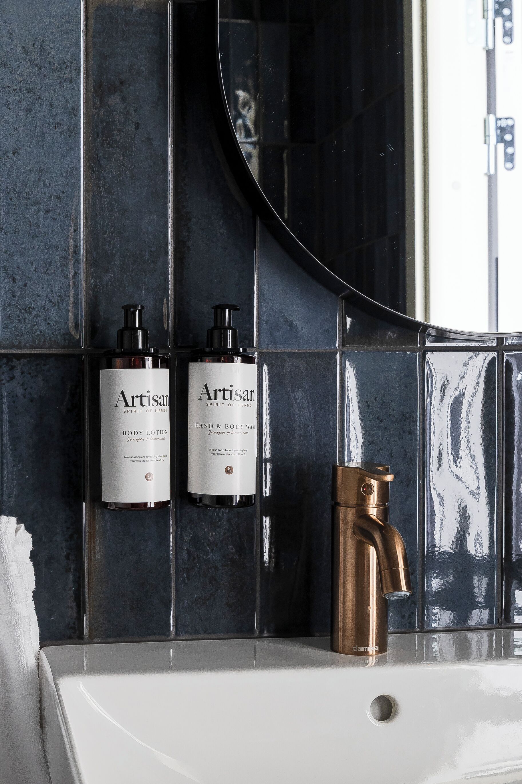 A bathroom with a white sink, a copper faucet, and two bottles of Artisan body lotion and hand & body wash.