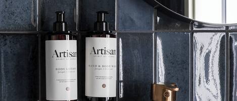 A bathroom with a white sink, a copper faucet, and two bottles of Artisan body lotion and hand & body wash.