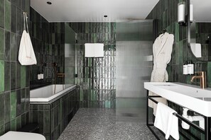 A modern bathroom with a bathtub, a vanity with a sink, and a mirror. There are towels hanging on the wall and a white bag hanging on a hook.