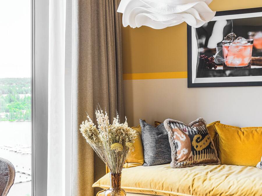 Een moderne woonkamer met een groot raam, een houten salontafel, een bank met gele kussens en een hanglamp.