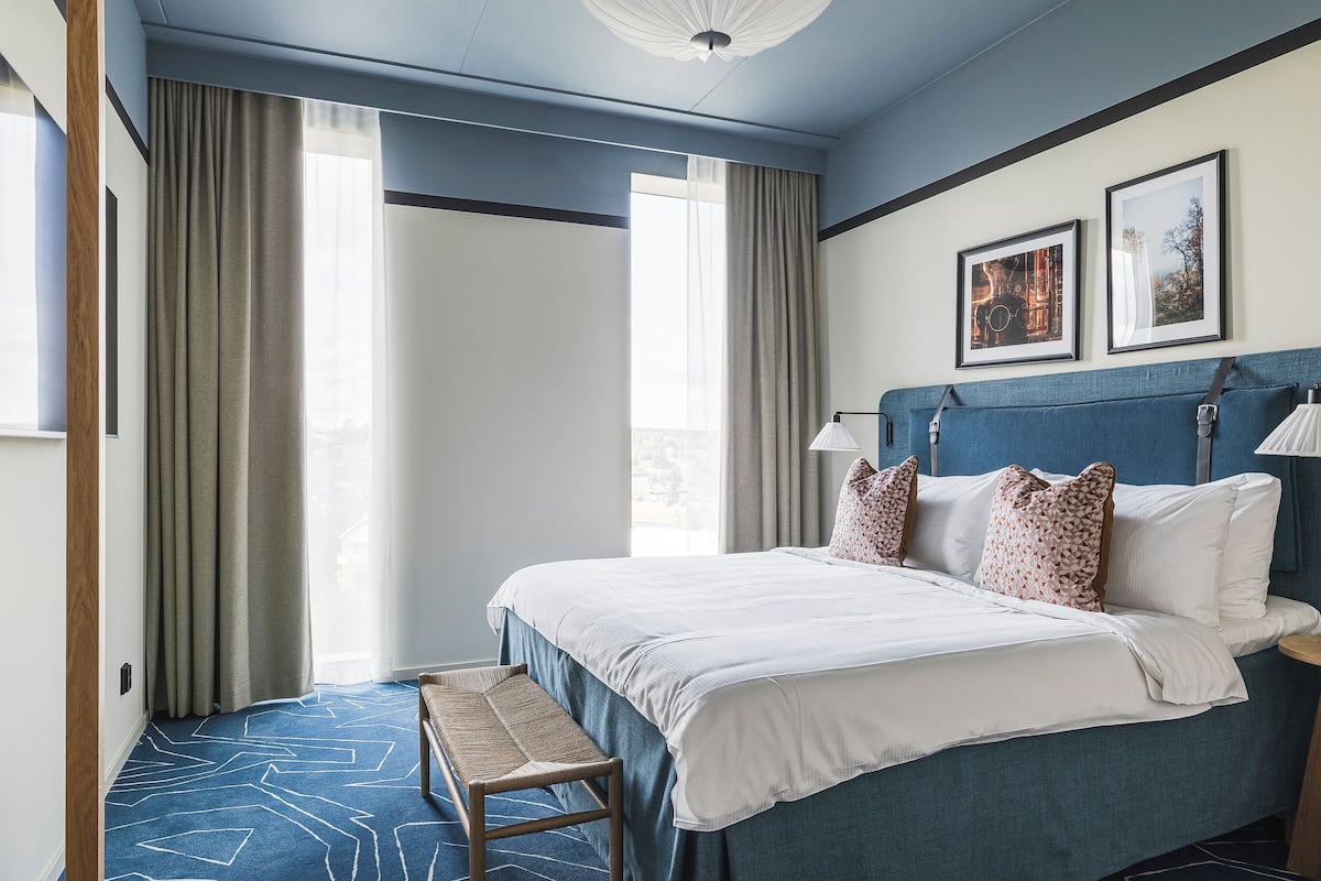 Une chambre d’hôtel avec un grand lit, un banc et deux tableaux encadrés au mur.