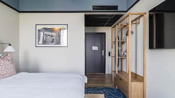 Ett hotellrum med en säng, en inramad tavla på väggen, en garderob i trä och en tv som är monterad på väggen.