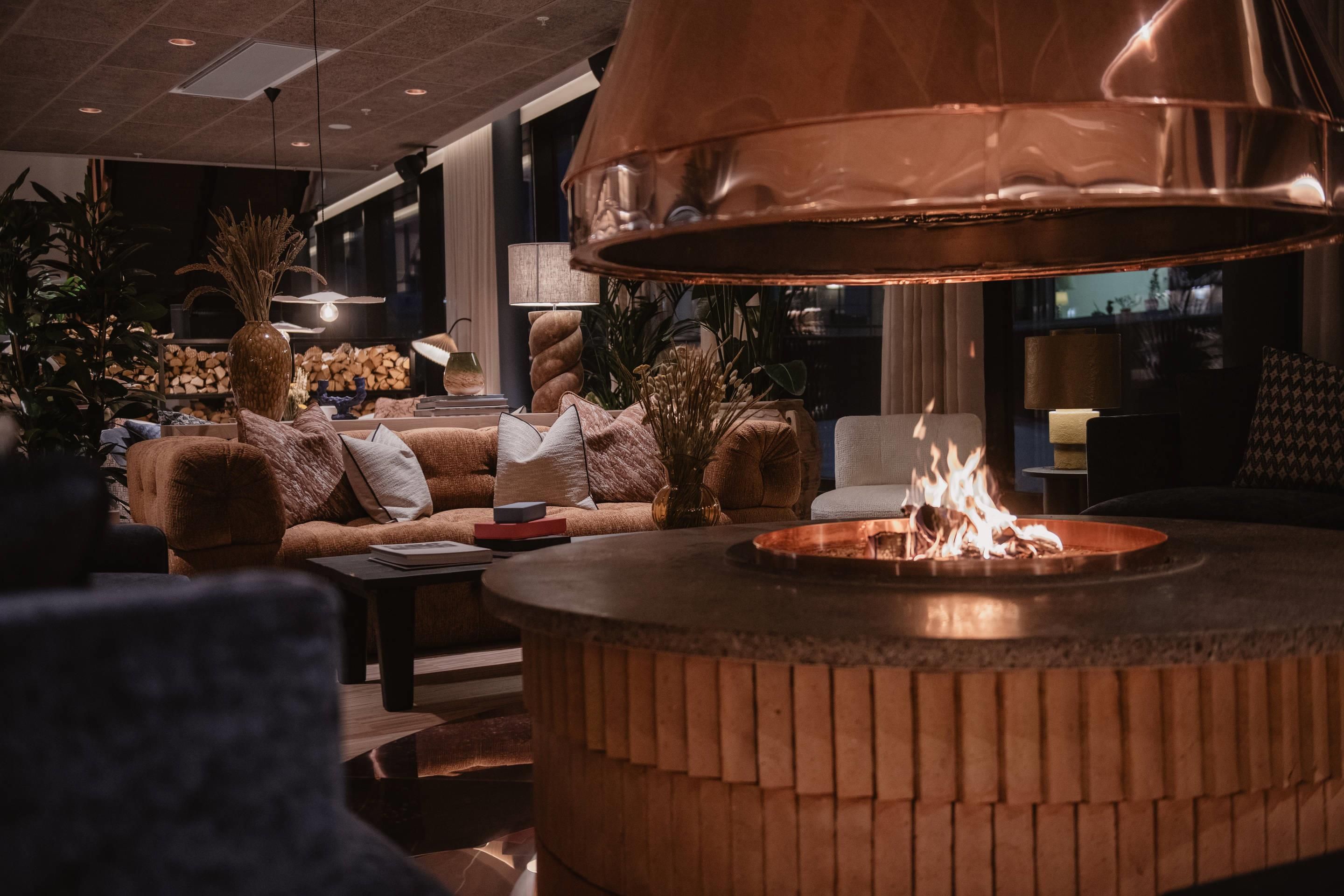 A cozy lounge area with a central fire feature, comfortable seating, and ambient lighting.