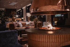 A cozy lounge area with a central fire feature, comfortable seating, and ambient lighting. - Hernö Gin Hotell (Harnosand)