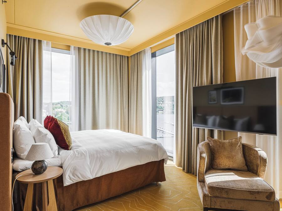 Habitación de hotel con una cama grande, televisión, sofá y vistas a la ciudad.