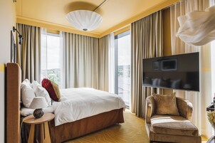 Quarto de hotel com uma cama grande, televisão, sofá e vista da cidade.