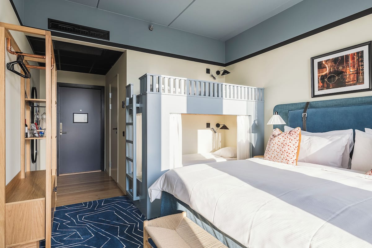 Une chambre d’hôtel avec un lit superposé, une armoire en bois, une table de chevet, une lampe et un tableau encadré au mur.