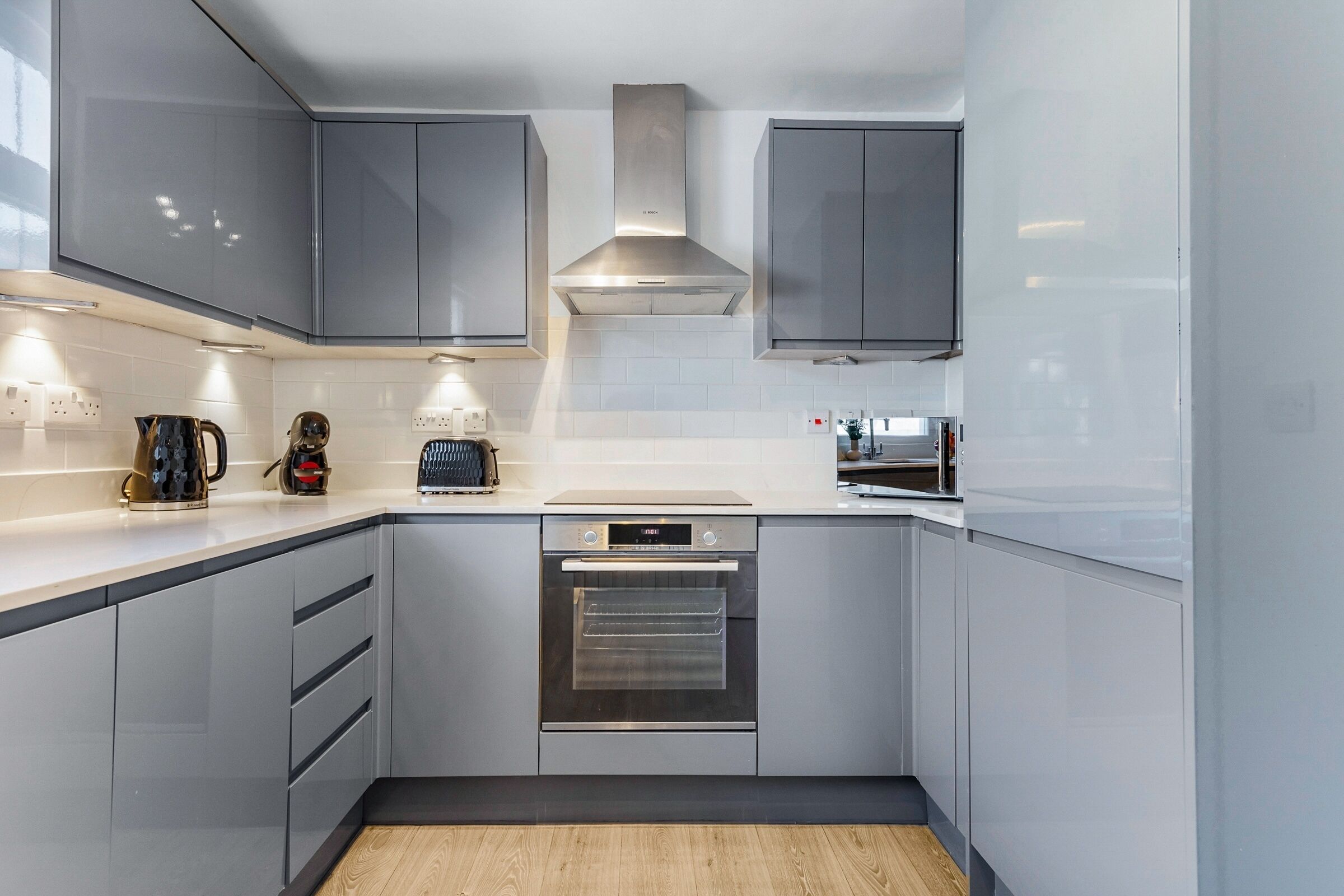 A modern kitchen with grey cabinets, a built-in oven, and a stainless steel range hood.
