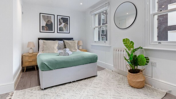 Une chambre moderne avec un lit, des tables de chevet, un grand miroir et une plante en pot.