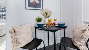 Un coin repas avec une table ronde, deux chaises, une plante en pot, un vase avec des fleurs séchées et une assiette de croissants.